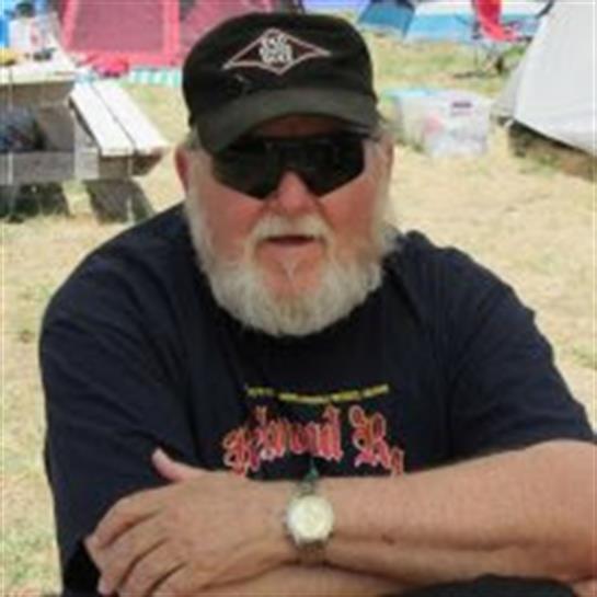 An older man with a beard relaxes outdoors, enjoying the warm weather and camping vibe.