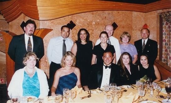 Colleagues and friends smile for a photo at a formal dinner, enjoying the evening together.