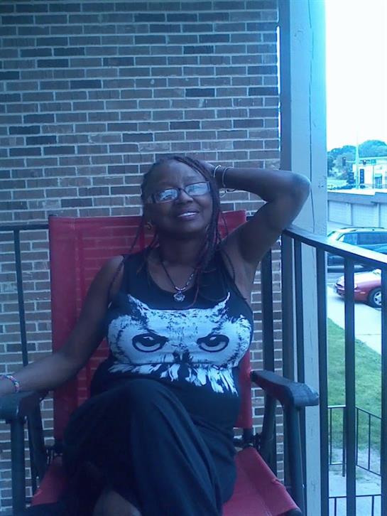 A joyful woman sits comfortably on a balcony enjoying the pleasant warmth of the sun.