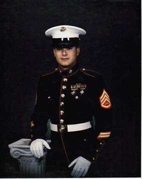 Enlisted Marine stands proudly in formal dress uniform with a stone pillar in the background.