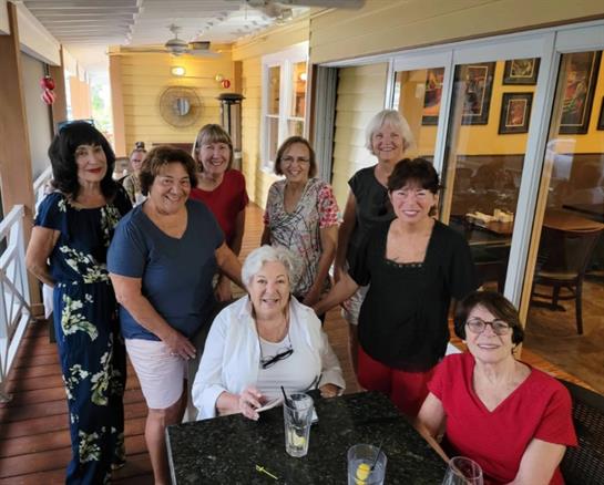 A group of eight women share laughter and stories over lunch at a restaurant.
