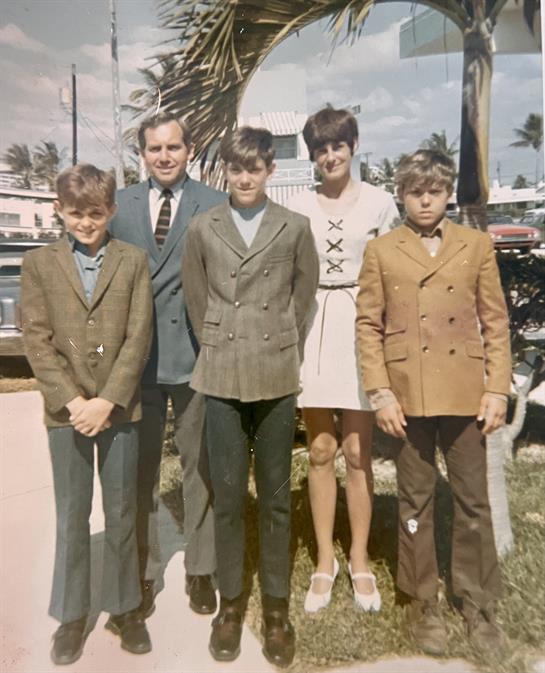 A group of five dressed in formal wear smiles for a family photo near the coast.