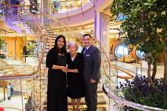 A family poses together in a luxurious cruise ship lobby with an elegant staircase.