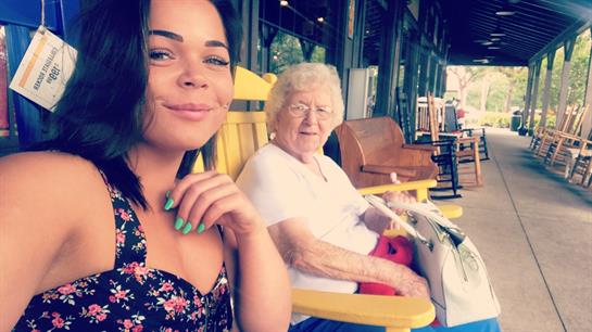 A young woman and an elderly lady sit in bright rocking chairs, enjoying a warm afternoon.