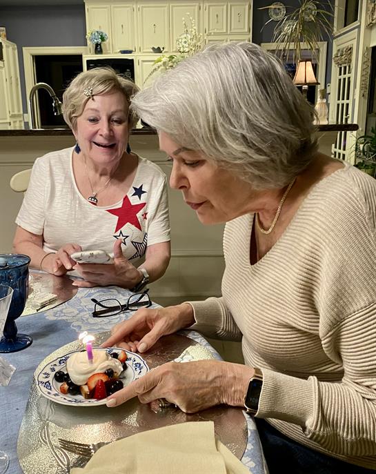 Two women enjoy a birthday dessert with berries and a candle in a cozy home setting.