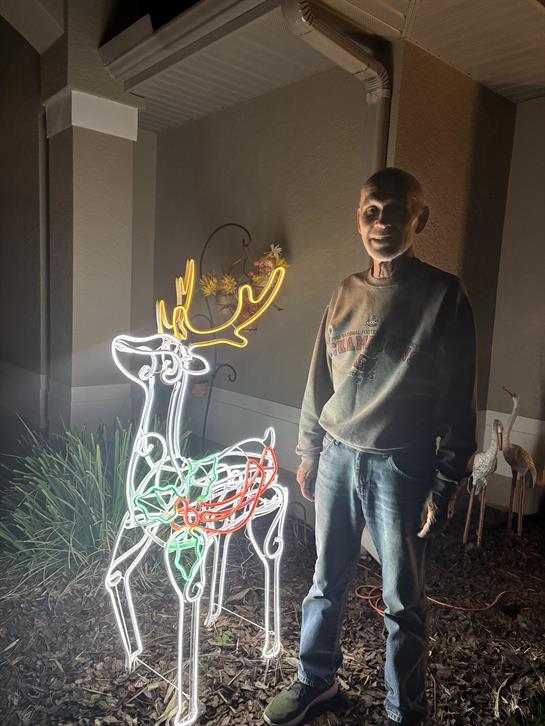 A man stands next to a bright, illuminated reindeer decoration in a yard at night.