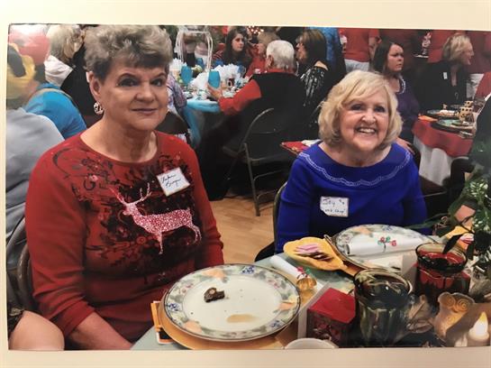 Two women sit at a table sharing smiles and conversation amid holiday decorations at the event.