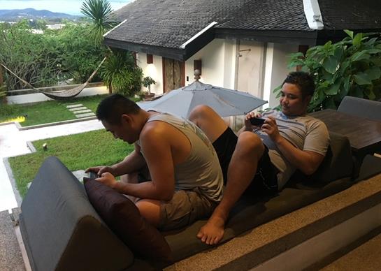 Two people sit comfortably on a balcony, enjoying the view while using their devices.