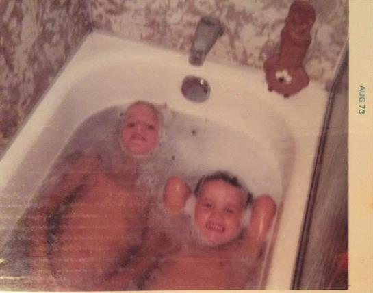 Two children are relaxing in a bathtub filled with water, smiling and having fun.