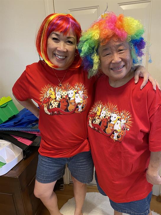 Two friends smile and pose together wearing bright costumes during a lively celebration.