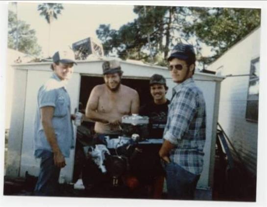 Four friends gather around a motorcycle in a garage, enjoying a sunny day together.