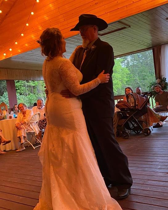 A couple dances joyfully on wooden floor amidst guests enjoying a summer wedding celebration.