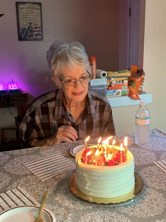 A woman is happily observing a birthday cake adorned with candles while sitting at a table.