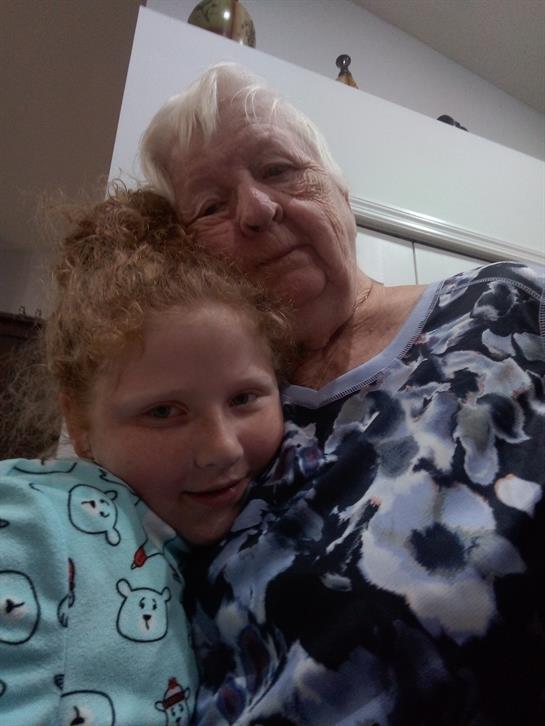 A young girl in pajamas embraces her grandmother, capturing a warm family bond indoors.