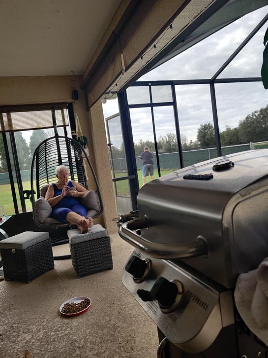 A person sits comfortably, enjoying a peaceful moment while another grills nearby.