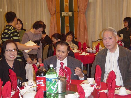 A lively gathering of individuals enjoying a meal at a banquet with red tablecloths and decorations.