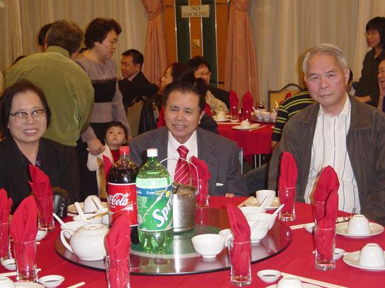 Family and friends gather at a round table, enjoying drinks and a festive meal.
