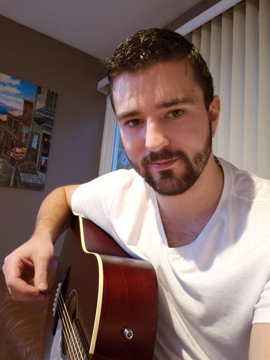 A musician strums his acoustic guitar, expressing creativity in a cozy indoor environment.