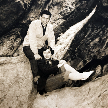 Two individuals share a joyful moment outdoors, surrounded by rocky formations, smiling happily.