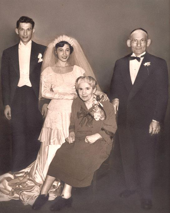 A bride and groom stand proudly with their family members in a formal wedding portrait.