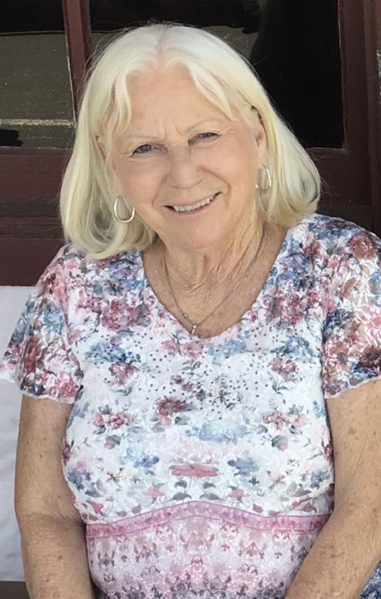 Elderly woman with light hair smiles happily while sitting outside on a warm afternoon.