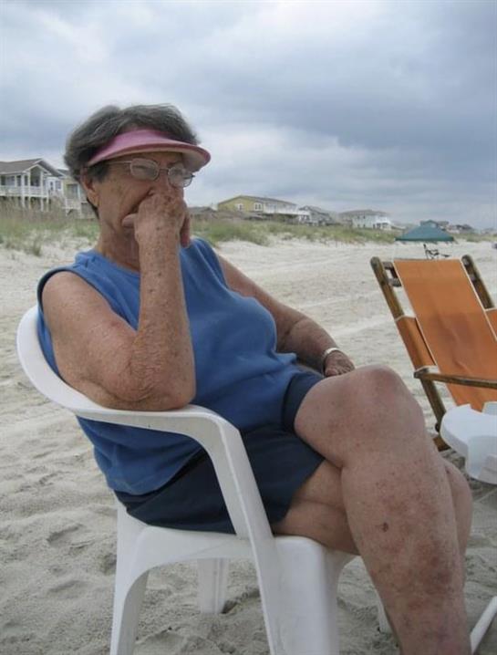 Relaxation on the beach as an older woman sits in a chair, deep in thought under cloudy skies.