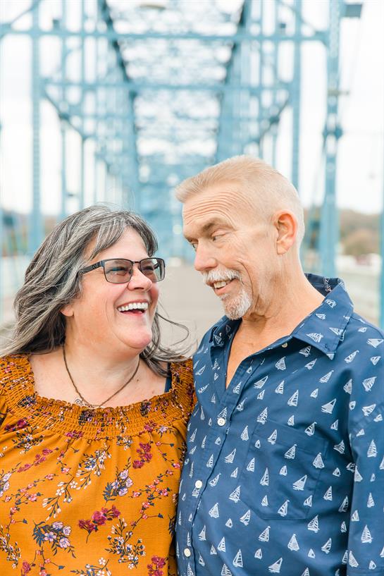 Two people share laughter and smiles, standing close together on a bridge, radiating happiness.