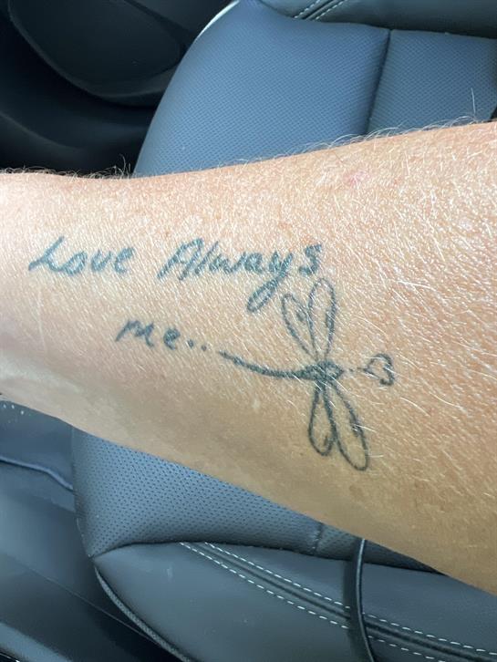 A heartfelt tattoo featuring the phrase love always me and a dragonfly design on an arm.