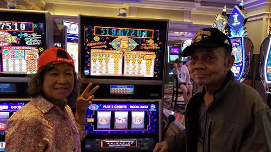 Two people happily pose by a slot machine after winning a jackpot in a vibrant casino.