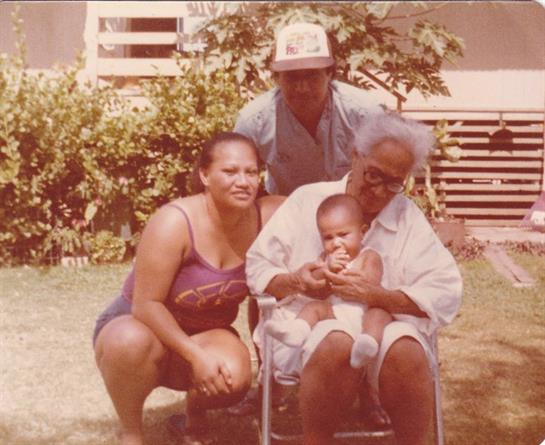 Three adults and a baby share smiles in a sunny backyard, creating a joyful family moment.