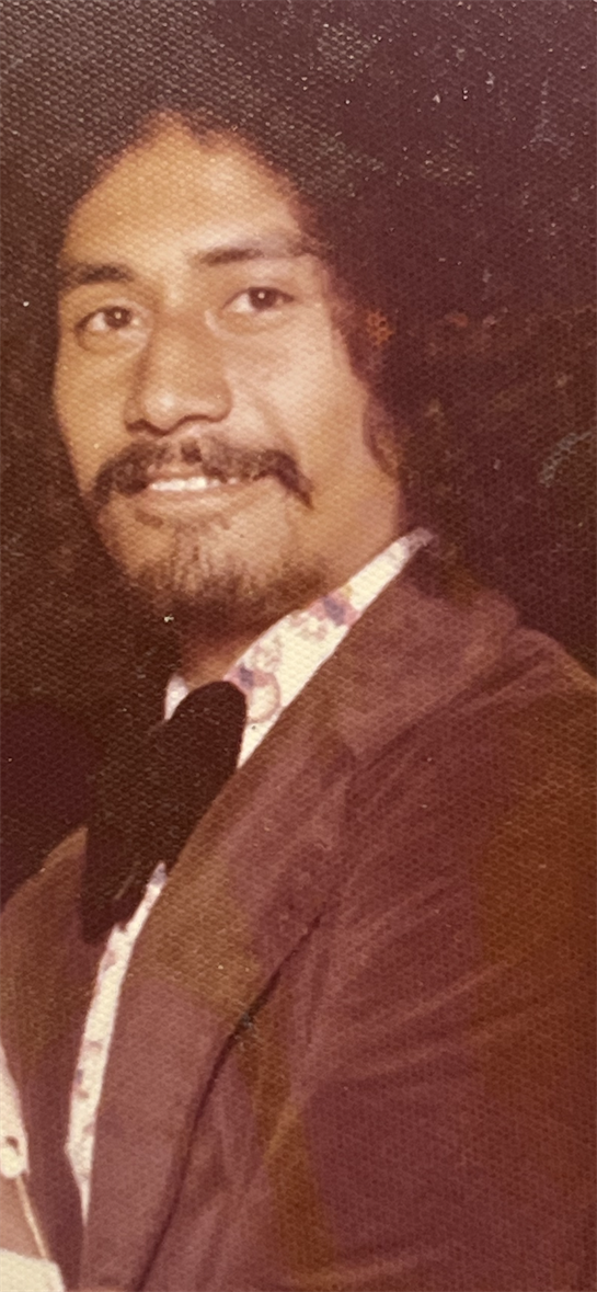 A smiling man with curly hair in vintage clothes poses confidently at a gathering.
