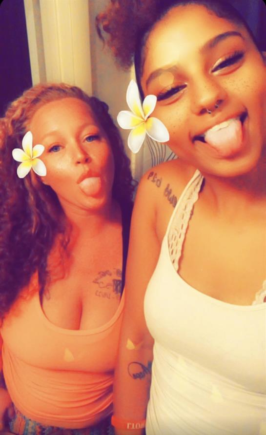 Two friends pose playfully with flowers on their faces, sharing laughter and joy indoors.