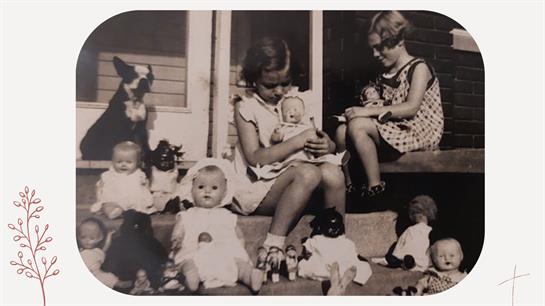 Two girls sit on the porch while holding and playing with various dolls surrounded by more dolls.