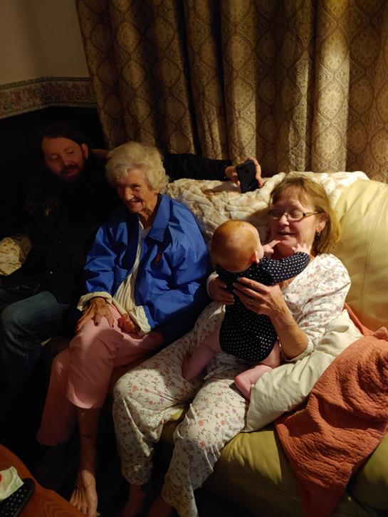 A warm family moment unfolds as three generations sit together, sharing smiles and cuddles.