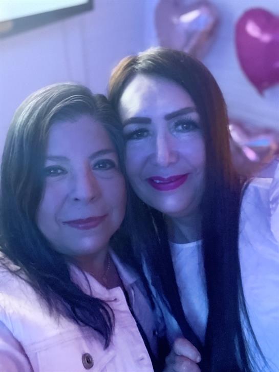 Two women smile warmly while celebrating at a lively event adorned with festive decor.