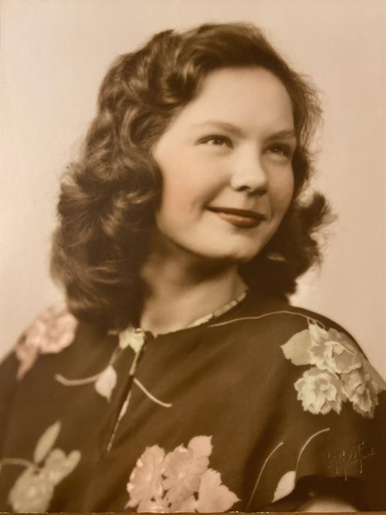 A young woman smiles warmly, showcasing her curly hair and floral dress in a timeless portrait.