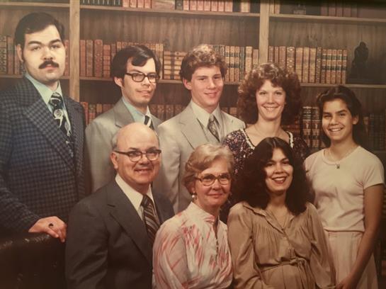 Family gathered in formal wear, smiling and posing in front of bookshelves filled with books.