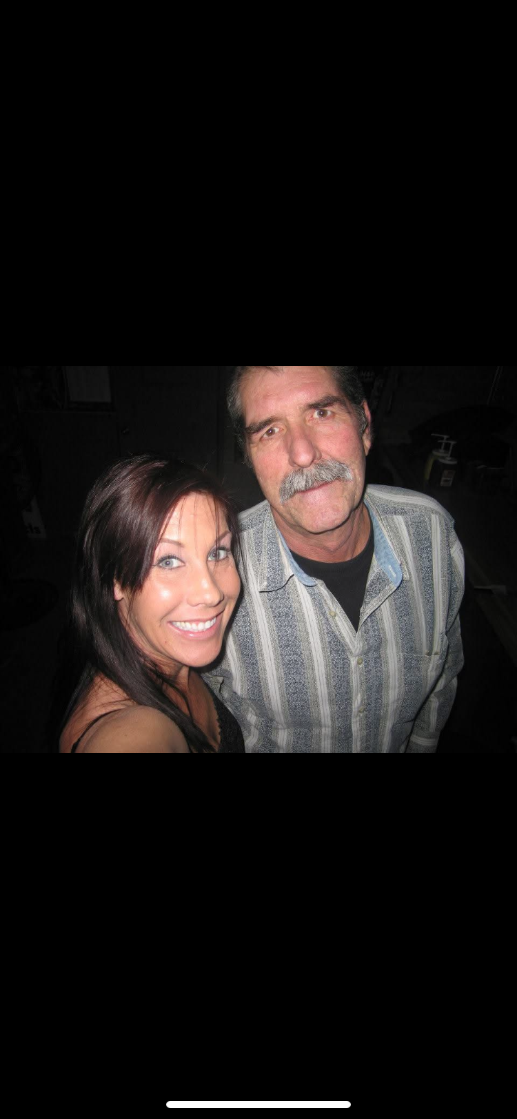 A woman and man share a cheerful smile in a relaxed indoor environment during the evening.