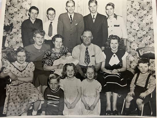 A large family poses together in a charming vintage home filled with patterned wallpaper.