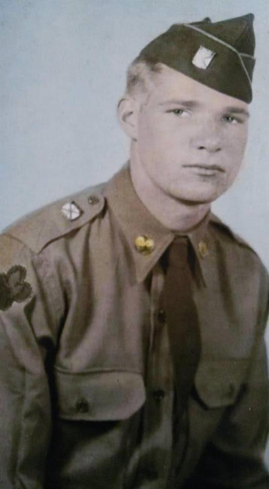 A young soldier dressed in khaki military uniform stands confidently for a portrait.