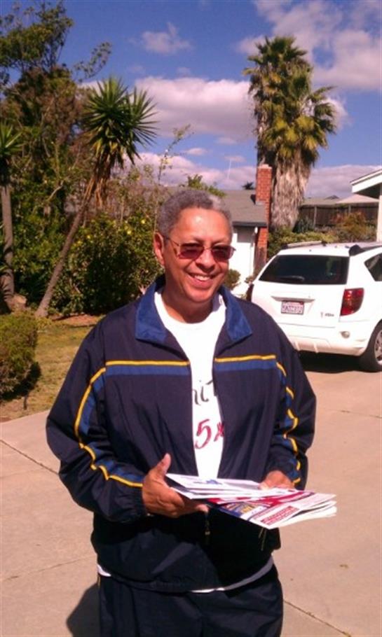 Man wearing sunglasses holds various newspapers while standing on a driveway.