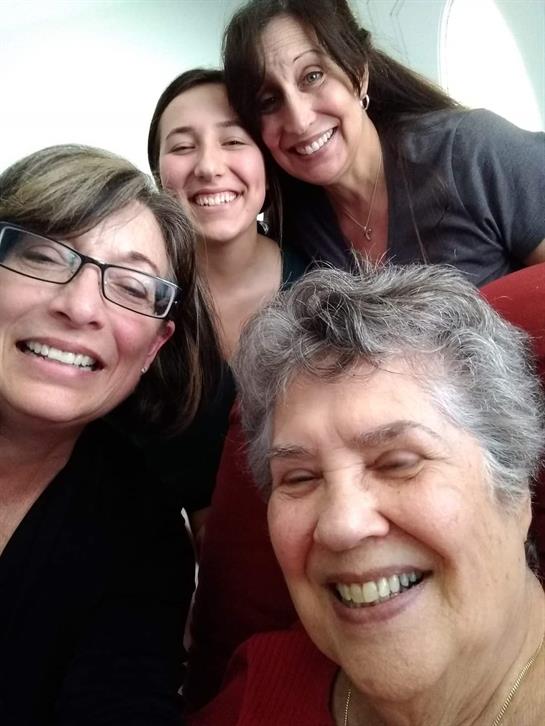 Four women share smiles and laughter while taking a selfie together at home.