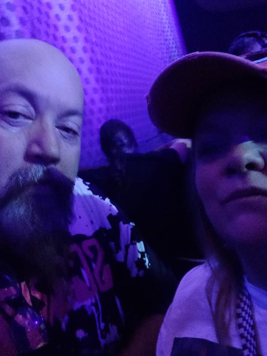 Two people pose closely together, illuminated by purple lights as they enjoy their night at a venue.