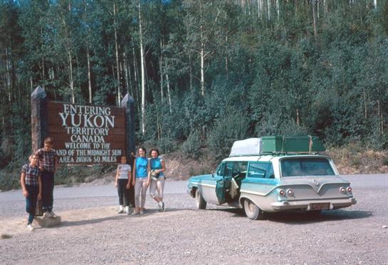 Group of friends enjoying a road trip at the Yukon border in summer, surrounded by trees.