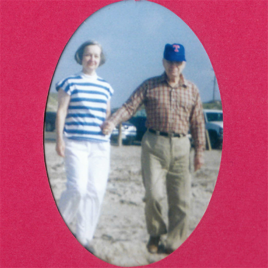 An elderly couple strolls together on the beach during a clear, sunny day, enjoying the moment.