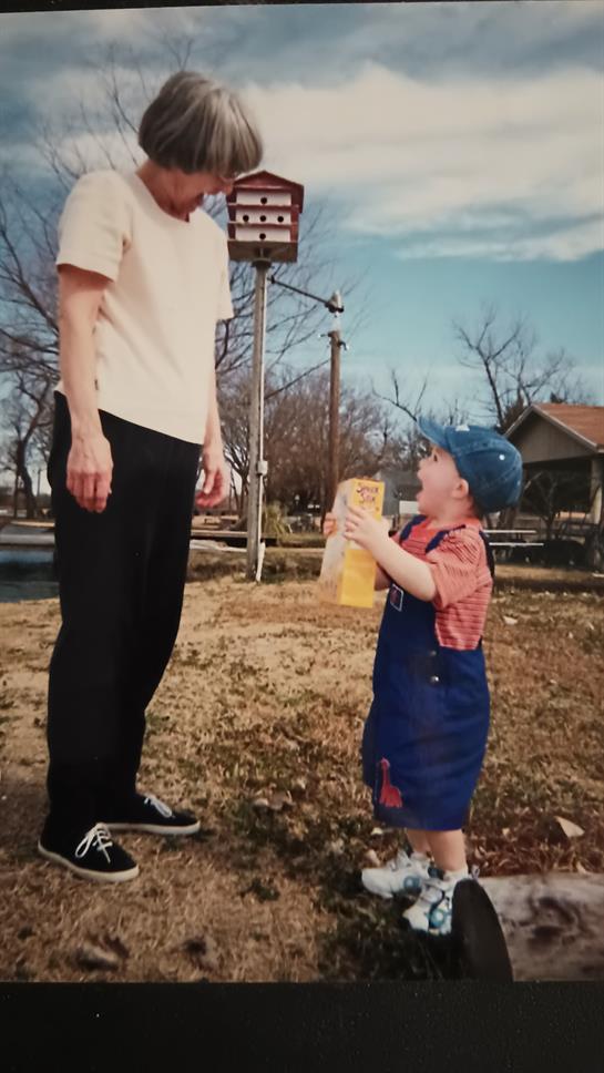 A young child excitedly engages with an adult, holding a snack in a sunlit outdoor area.
