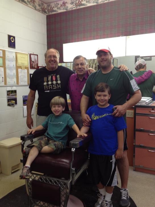 A cheerful family poses together in a barbershop, showcasing their bond across generations.
