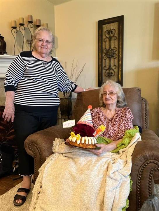 Two women gather around a decorated birthday cake in a warm and inviting living room.