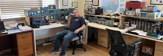 A man sits at his desk, using a microphone in his personal radio station.