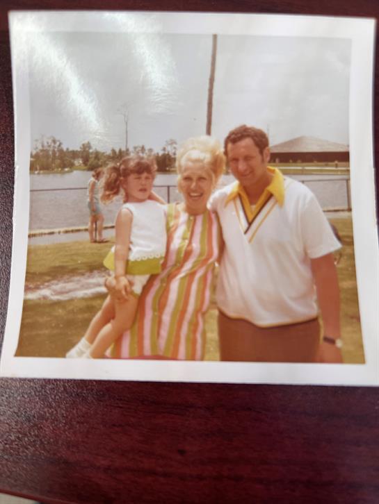 A little girl is held by a woman while a man stands beside them, all smiling happily.